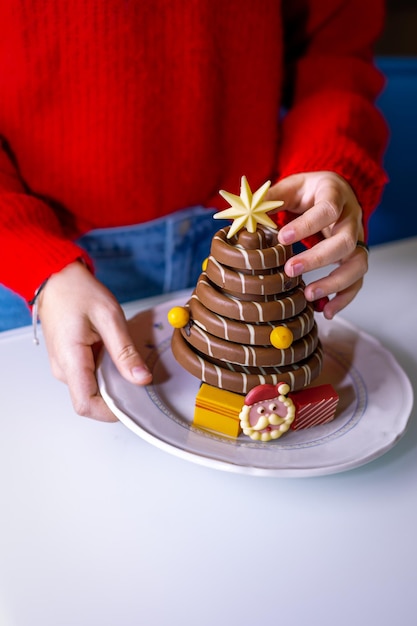 Weibliche Hände halten einen Teller mit 3D-Dessertschokolade in Form eines Weihnachtsbaums und eines Weihnachtsmanns