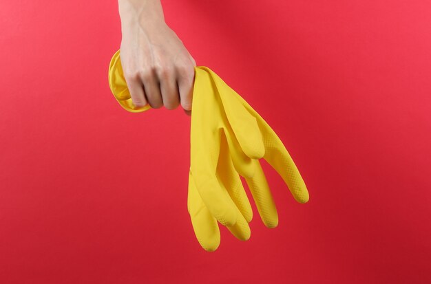 Weibliche Hände halten gelbe Handschuhe zum Reinigen auf einem roten Hintergrund. Hausreinigungskonzept