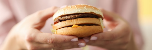 Weibliche Hände halten Hamburger mit Käse und Fleisch