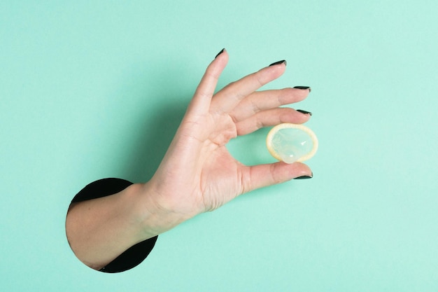 Weibliche Hände halten Kondom durch ein Loch auf neonminzfarbenem Hintergrund Konzept für sicheren anonymen Sex