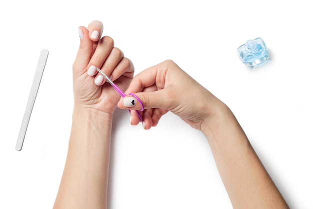 Weibliche Hände halten Nagelscheren, neben Geräten für die Nagelpflege. Das Mädchen macht eine Maniküre. isoliert auf weißem Hintergrund. Von oben betrachten. Hochwertiges Foto