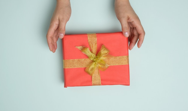Weibliche Hände halten rote Geschenkbox auf blauem Hintergrund, Konzept der Glückwünsche