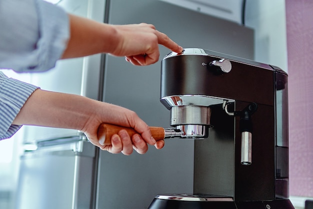 Weibliche Hände halten Siebträger und machen frischen aromatischen Kaffee zu Hause unter Verwendung einer modernen Kaffeemaschine