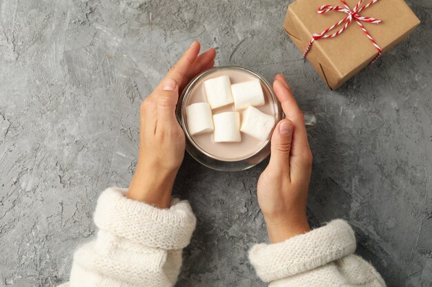 Weibliche Hände halten Tasse Kaffee mit Marshmallows auf grauem Hintergrund, Draufsicht