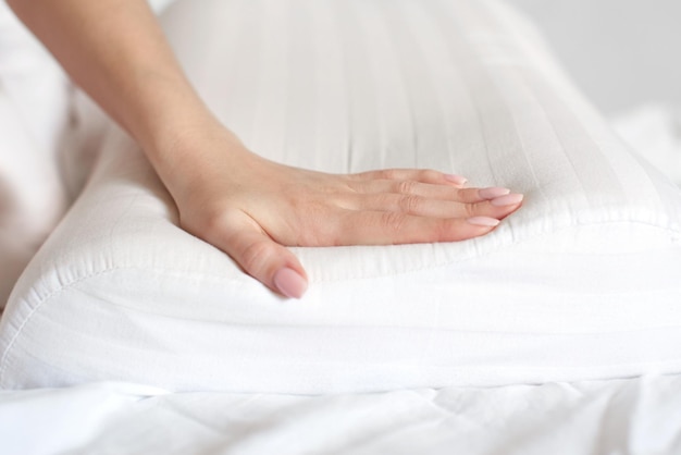 Weibliche Hände halten und zeigen ein orthopädisches Kissen auf einem weißen Bett. Bequemer Schlaf und gesunde Wirbelsäule