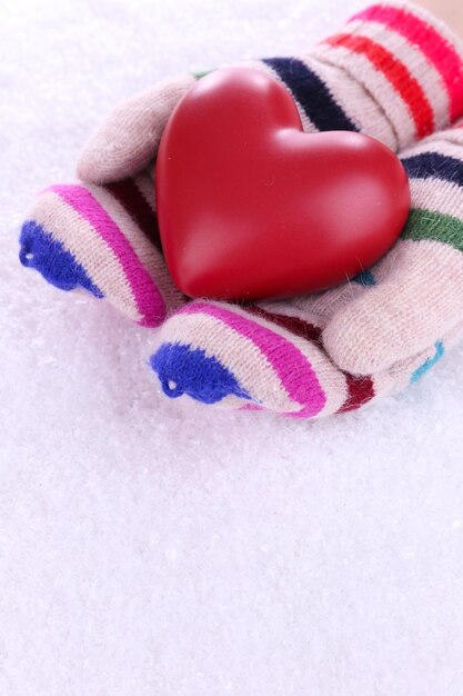 Weibliche Hände in Fäustlingen mit Herz auf Schneehintergrund