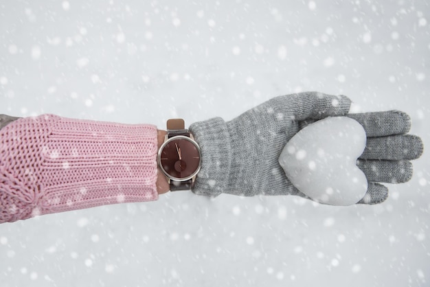 Weibliche Hände in gestrickten Fäustlingen mit Herz aus Schnee in Schönheit Wintertag Liebe oder Valentinstag Konzept