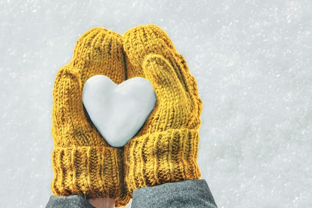 Weibliche Hände in gestrickten Handschuhen mit einem Herzen aus Schnee an einem Wintertag Liebeskonzept