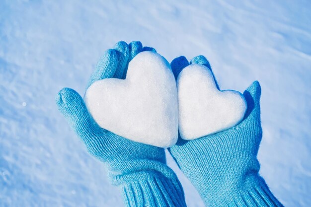 Weibliche Hände in gestrickten Handschuhen mit Herzen aus Schnee an einem Wintertag Liebeskonzept