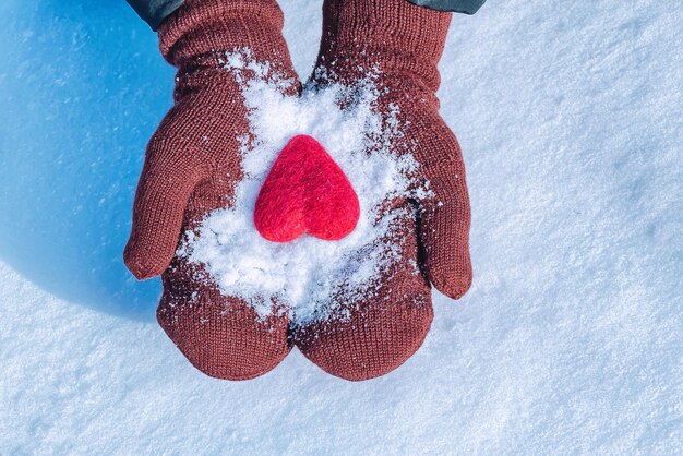 Weibliche Hände in gestrickten Handschuhen mit rotem Herzen an einem Wintertag Liebeskonzept