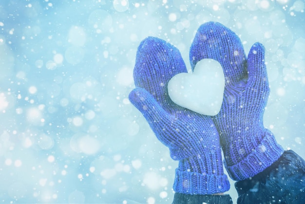 weibliche hände in gestrickten handschuhen mit schneeherz am wintertag. Liebeskonzept.