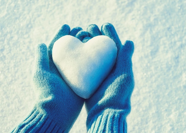 Weibliche Hände in gestrickten Handschuhen mit Schneeherzen am Wintertag. Liebeskonzept. Valentinstag Hintergrund