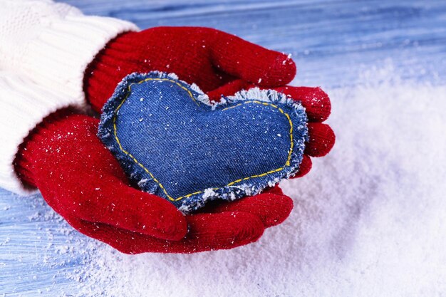Weibliche Hände in Handschuhen mit dekorativem Herzen auf Schneehintergrund snow