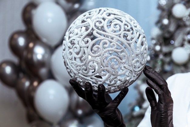 Weibliche hände in schwarzen medizinischen handschuhen halten einen silbernen ballon vor dem hintergrund