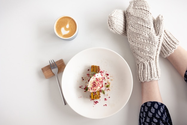 Weibliche Hände in weißen Handschuhen mit Kuchen und Kaffee auf weißem Tisch mit Kuchen. Konzept von Winter, Wärme, Feiertagen, Ereignissen.