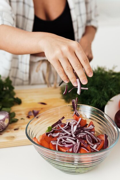 Weibliche Hände kochen vegetarischen Salat und fügen rote Zwiebeln hinzu
