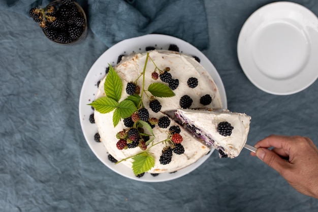 Weibliche Hände legen ein Stück hausgemachten Kuchen mit Brombeeren auf einer Untertasse aus