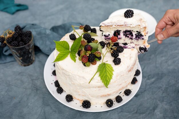 Weibliche Hände legen ein Stück hausgemachten Kuchen mit Brombeeren auf einer Untertasse aus.