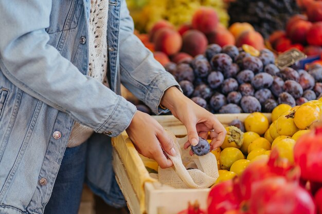 Weibliche Hände legen Obst und Gemüse in Baumwollbeutel auf dem Lebensmittelmarkt. Wiederverwendbare Öko-Tasche zum Einkaufen. Nachhaltiger Lebensstil. Umweltfreundliches Konzept.