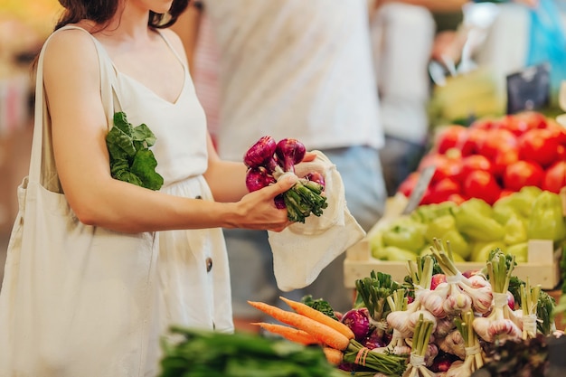 Weibliche Hände legen Obst und Gemüse in Baumwollbeutel auf dem Lebensmittelmarkt. Wiederverwendbare Öko-Tasche zum Einkaufen. Zero-Waste-Konzept.