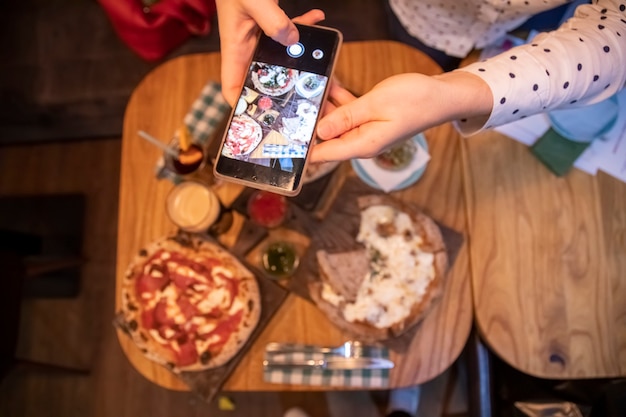 Weibliche Hände machen Fotos auf einem Smartphone-Tisch mit einer leckeren Pizza in einem Restaurant