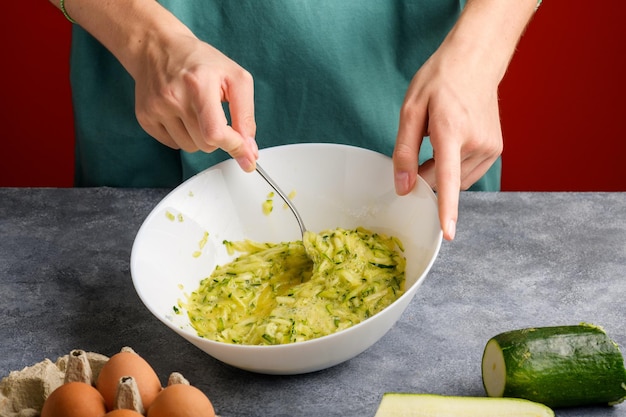 Weibliche Hände mischen mit Gabel geschlagenen Eiern und geriebenen Zucchini in einer Glasschüssel