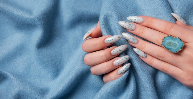 Weibliche Hände mit blauem Nageldesign auf blauem Textilgrund