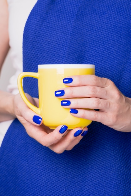 Weibliche Hände mit blauer Nagelmaniküre, die gelbe Tasse hält