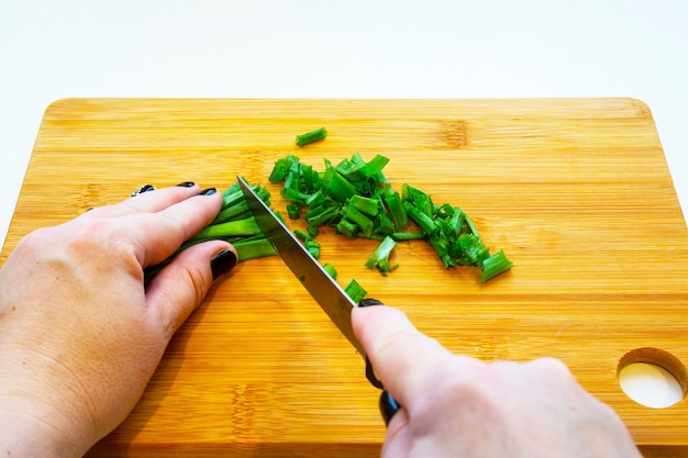 Weibliche Hände mit einem Messer, Gemüse auf einem Holzbrett auf weißem Hintergrund schneiden. Frau schneidet Frühlingszwiebeln