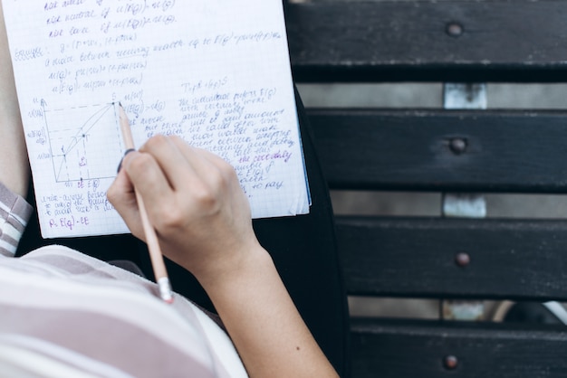 Foto weibliche hände mit einem notizbuch und stift, auf hölzernen braunen bank, draufsicht