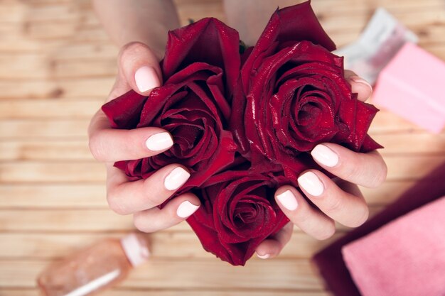 Weibliche Hände mit Maniküre halten rote Rosen