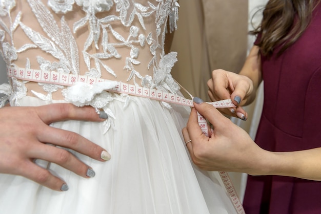 Weibliche Hände mit Maßband an der Taille des Hochzeitskleides