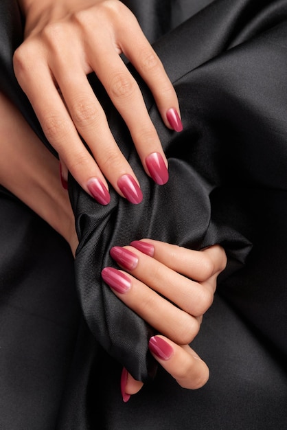 Weibliche Hände mit rosafarbenen Nägeln, die einen schwarzen Satinstoff halten