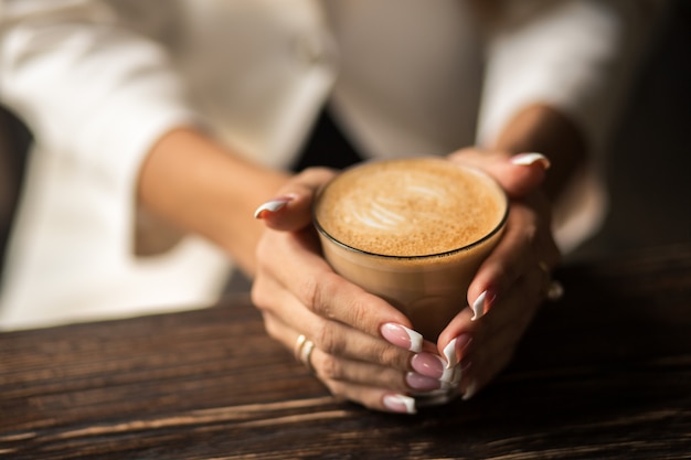 Weibliche Hände mit schöner Manikürenahaufnahme halten eine Schale mit heißem Kaffee auf einem Holztisch.