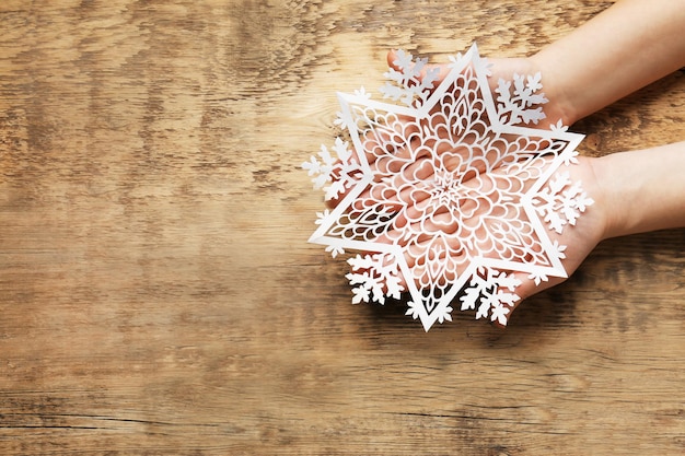 Weibliche Hände mit schöner Papierschneeflocke auf hölzernem Hintergrund