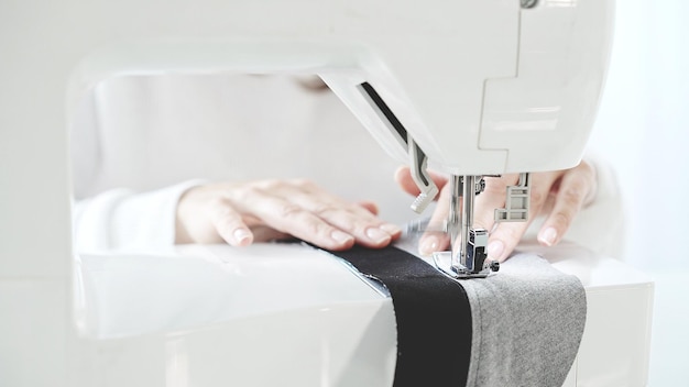 Weibliche Hände nähen grauen Stoff auf einer weißen Nähmaschine in der Nähe