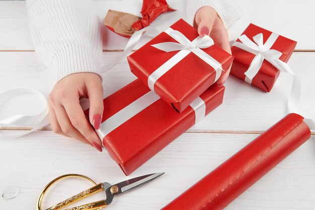 Weibliche Hände nehmen oder verpacken Weihnachten, Geburtstag oder Valentinstag rotes Geschenk auf weißem Hintergrund, Nahaufnahme. Ferien- und Verkaufssaison