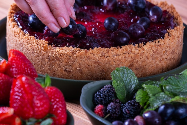 weibliche Hände schmücken einen Beerenkuchen mit Früchten