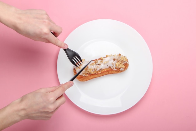 Weibliche Hände schneiden Eclair auf einem Teller