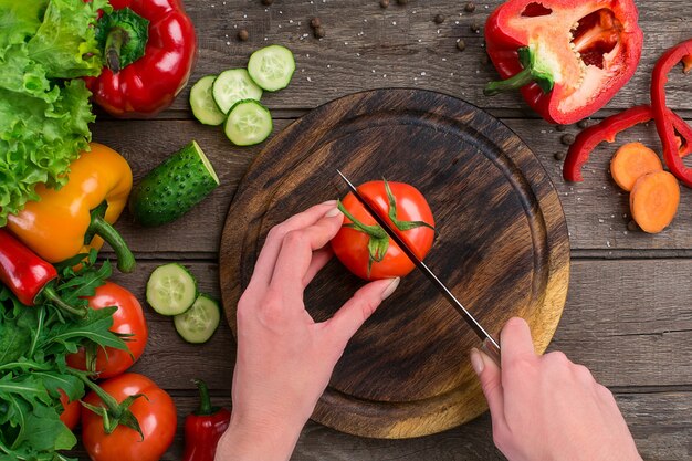 Weibliche Hände schneiden Tomaten am Tisch, Ansicht von oben. Auf dem Tisch Gemüse und ein Holzbrett