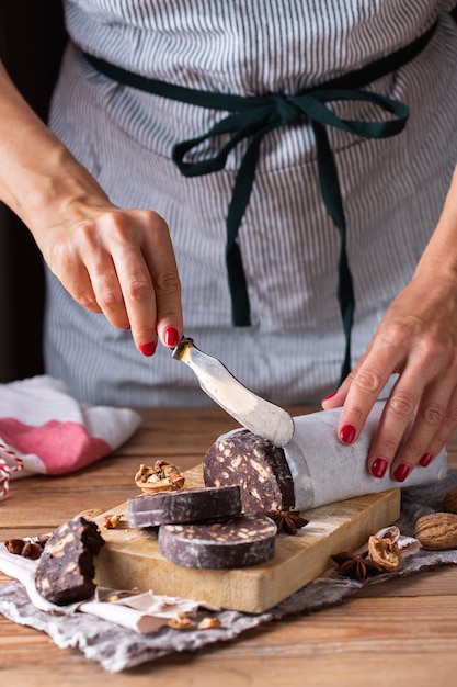 Weibliche Hände schneiden traditionelle italienische Dessertweihnachtsschokoladesalami