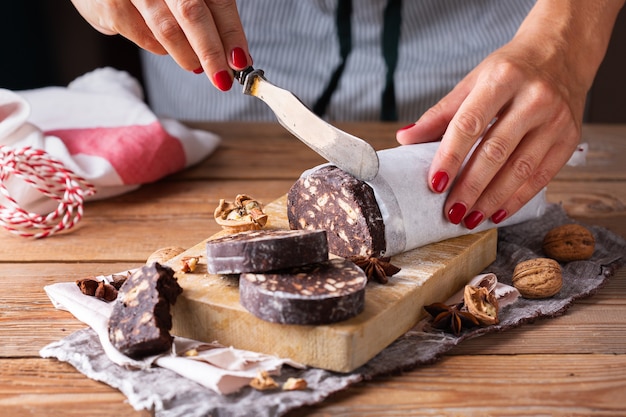 Foto weibliche hände schneiden traditionelles italienisches dessert - weihnachtsschokoladensalami mit gebrochenen keksen und walnüssen auf einem tisch