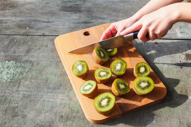 Weibliche Hände schnitten Kiwi auf einem Schneidebrett auf grauem Weinlesehintergrund