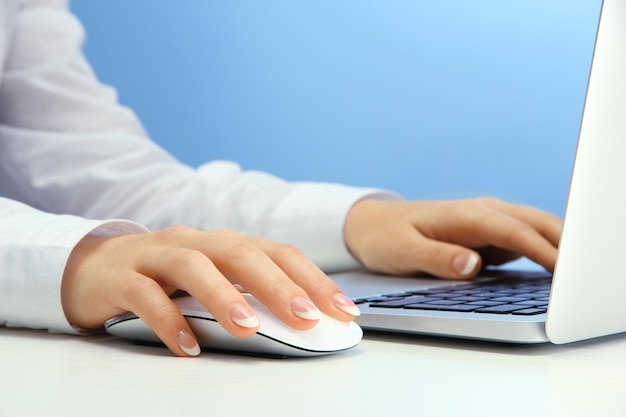 Weibliche Hände schreiben auf Laptop auf blauem Hintergrund