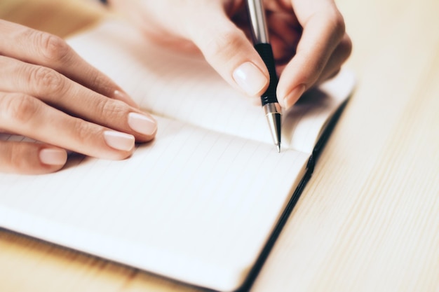 Weibliche Hände schreiben in Notizbuch mit Stift auf Holztisch