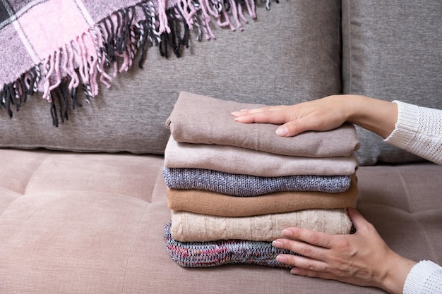 Weibliche Hände stapeln gemütliche Strickpullover auf dem Sofa mit Decke Warmes Konzept