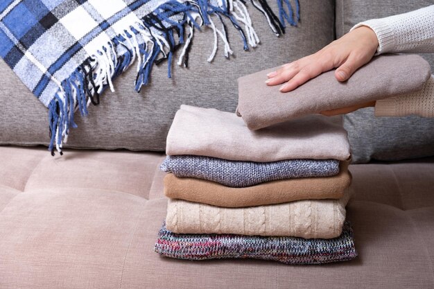 Weibliche Hände stapeln gemütliche Strickpullover auf dem Sofa Warmes Konzept
