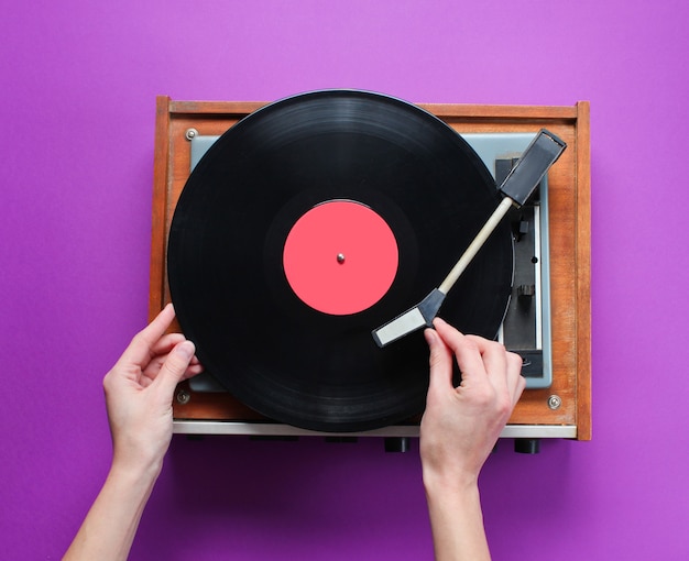 Weibliche Hände stellten Retro-Vinyl-Plattenspieler mit Platte auf lila Hintergrund auf