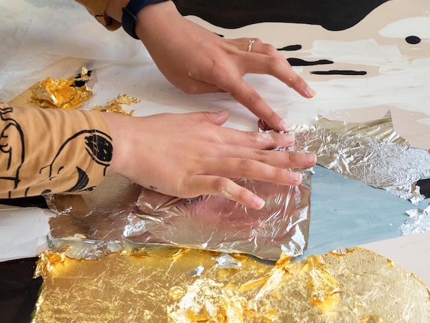 Weibliche Hände tragen Gold- und Silberpotal auf das Bild auf Potal-Maltechnik, bei der Blattgoldpartikel auf eine Innenmalerei aufgetragen werden