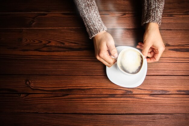 Weibliche Hände und Kaffee auf hölzernem Hintergrund